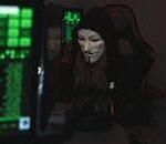 A mysterious hacker wearing a Guy Fawkes mask and black hoodie in a dimly lit room focused on computer screens.